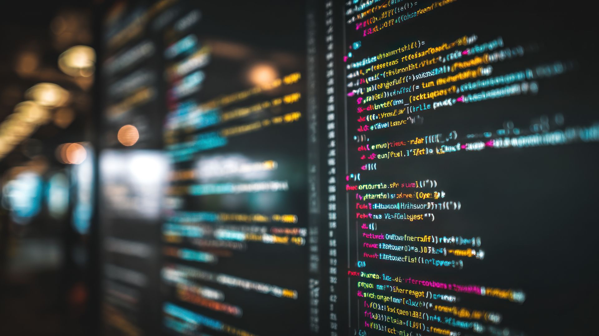 A computer screen displays colorful lines of code with a blurred background.